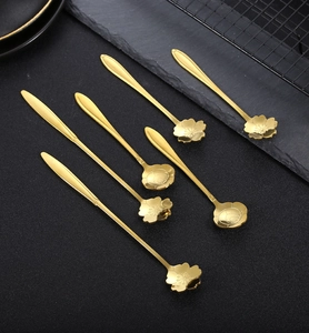 Detailed view of six golden floral stainless steel spoons on a black slate background