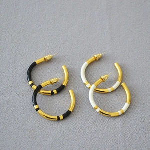 Detailed top view of C-shaped brass earrings with black and white enamel in gold finish