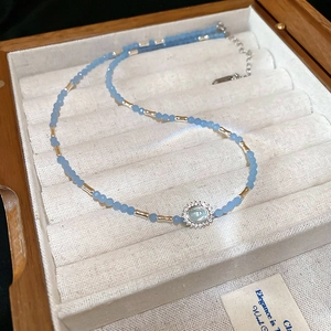 Detail of light blue beaded necklace with sunflower pendant on beige velvet jewelry box
