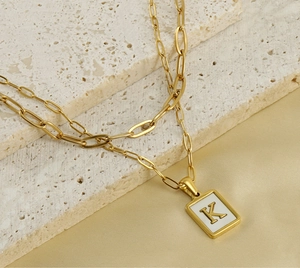 Macro detail of gold double-layer paperclip chain with rectangular initial K pendant
