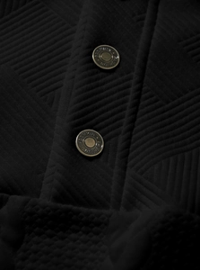 Detailed close-up of black textured fabric with vintage copper fashion buttons