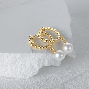 Macro detail of gold beaded earrings with white pearl pendant on minimalist stone base