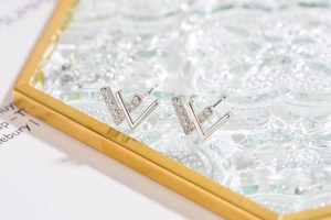 Close-up of silver W-shaped stud earrings with pavé zircons on a glass tray
