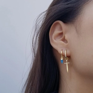 Detail of gold S925 silver dagger and cross earrings with blue stones on a model's ear