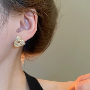 Close-up of model wearing gold crisscross triangle stud earrings with zircon stones