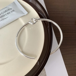 Minimalist S925 sterling silver interlocking knot bangle on a ceramic display