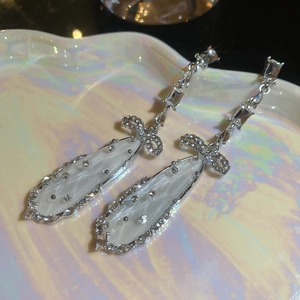 Macro detail of silver bow earrings with zircon stones and pearly waterdrop pendants