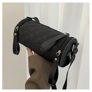 Detailed close-up of a black quilted cylindrical crossbody bag with a wide fabric strap