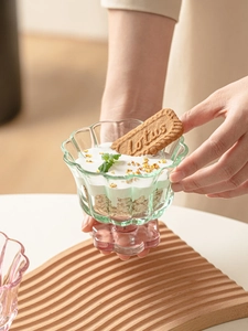 Détail d'une coupe en verre en forme de pétale avec yaourt et granola en mains