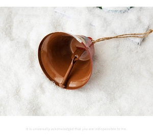 Close-up of red metal Christmas bell with Santa pattern and jute rope on snowy background