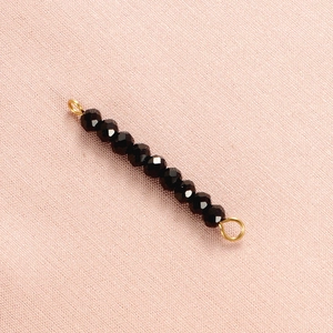Detail of faceted black crystal beads with gold metal connectors on pink fabric