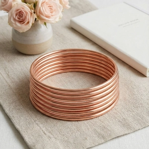 Set of stackable rose gold 3mm stainless steel bangles on minimalist linen surface