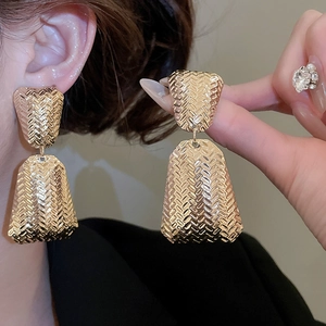 Detail of gold textured drop earrings showing woven metal design on model and in hand