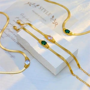 Golden snake chain jewelry set with green and purple gemstones on a white stone background