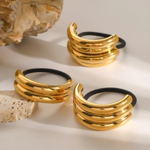 Minimalist gold stainless steel hair ties set with layered metal accents on stone background