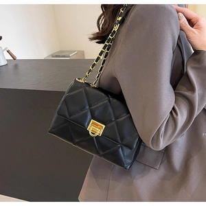 Detail of black quilted leather shoulder bag with gold hardware and chain strap on model