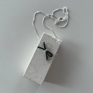 Close-up of black beaded bow pendant on a fine silver chain over grey stone
