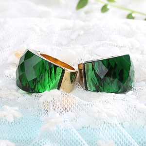 Close-up of a large faceted green crystal gemstone set in a bold gold plated metal ring