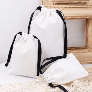 Detailed view of three white canvas drawstring gift bags with black ribbon ties