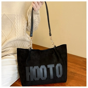 Close-up of black tote bag featuring soft suede texture and stylish metal chain strap