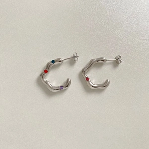 Macro detail of silver-colored wavy C-shape earrings with colorful inset gemstones