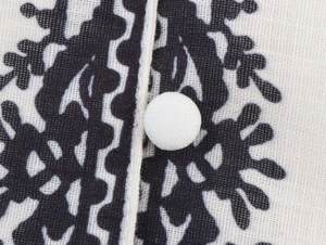 Detail view of a black botanical print on fabric with a single white button and stitching