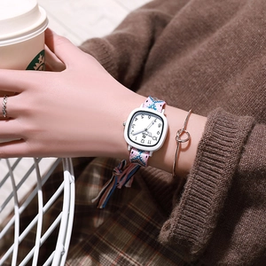 Detail of square quartz watch with pink and blue woven tassel strap and arabic numerals