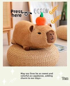 Plush Capybara toy with orange on head shown on a woven mat in a home setting