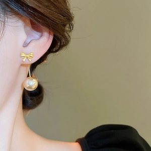 Detailed close-up of gold bow earrings with dangling champagne pearls on model