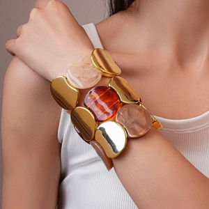 Dettaglio di un bracciale elastico largo con segmenti in metallo dorato e resina
