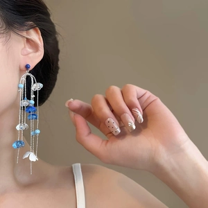 Close-up of elegant silver needle earrings featuring blue glass beads and white flowers