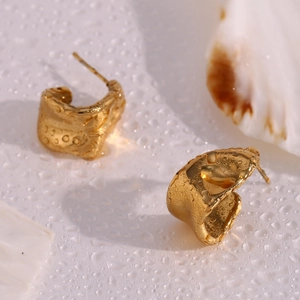 Detailed view of gold irregular textured earrings on a wet surface with white seashells