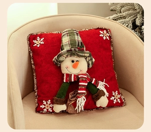 Detail of red Christmas pillowcase featuring a 3D snowman with green plaid hat on an armchair