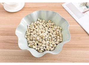 Detail of light blue lotus leaf fruit plate filled with pistachios on wooden table