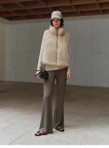 Chic beige faux fox fur vest styled with brown trousers in a minimalist city setting