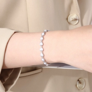 Detailed view of silver heart-shaped bracelet with white inlay worn over a beige sleeve