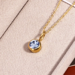 Macro shot of gold necklace with round blue birthstone pendant on beige velvet