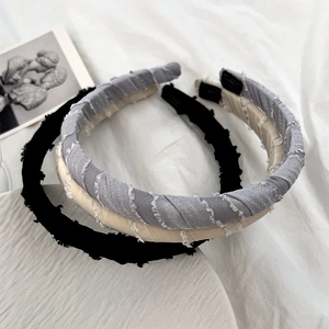 Three padded fabric headbands in grey, beige, and black colors on a white linen surface