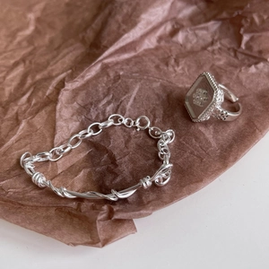 Macro detail of hand-woven S925 sterling silver twisted chain bracelet and square floral ring
