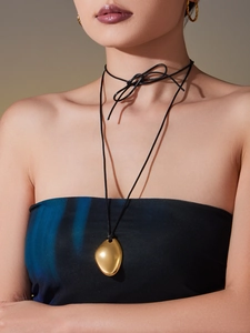 Detail showing polished gold pebble pendant on a black cord necklace with minimalist style