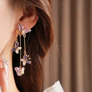 Gros plan de boucles d'oreilles papillon dorées avec cristaux violets portées par un mannequin