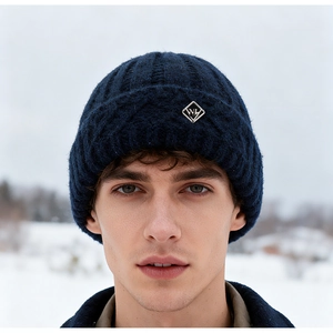 Detail of navy knit beanie featuring a diamond metal logo plate in a snowy outdoor setting
