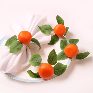 Artificial orange napkin rings with green leaves on white napkins for table decoration