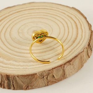 Detail of 18K gold-plated heart ring with green gemstone on rustic wood base