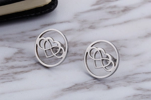 Close-up of silver hollow round earrings with interlocking heart patterns on marble background