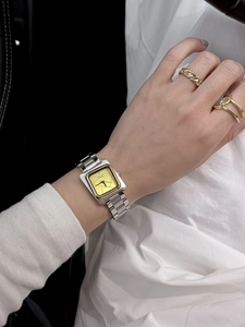 Détail d'une montre carrée dorée avec bracelet en acier inoxydable sur poignet féminin