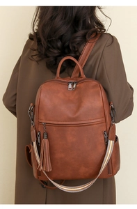 Detailed back view of a vintage brown leather backpack with tassel and striped strap