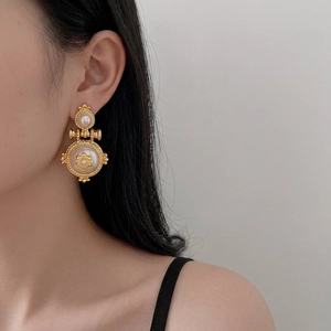 Vintage baroque pearl drop earrings in gold metal finish worn by model on grey background