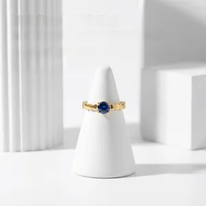 Detail of 18K gold-plated wavy ring featuring a deep blue sapphire zircon on a white stand