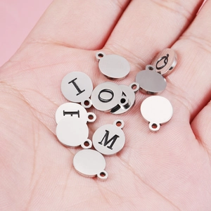 Mirror stainless steel round alphabet charms with A-Z letters held in palm on pink background